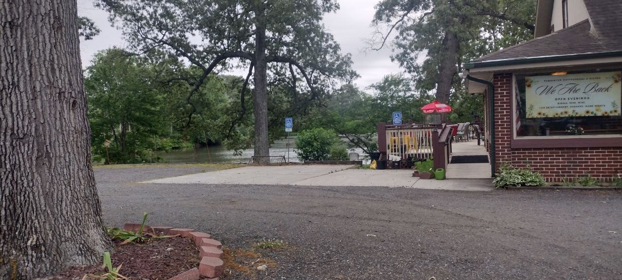 Pemberton Coffeehouse side view — gravel drive with the pond on the left and the wooden deck with a red umbrella on the right