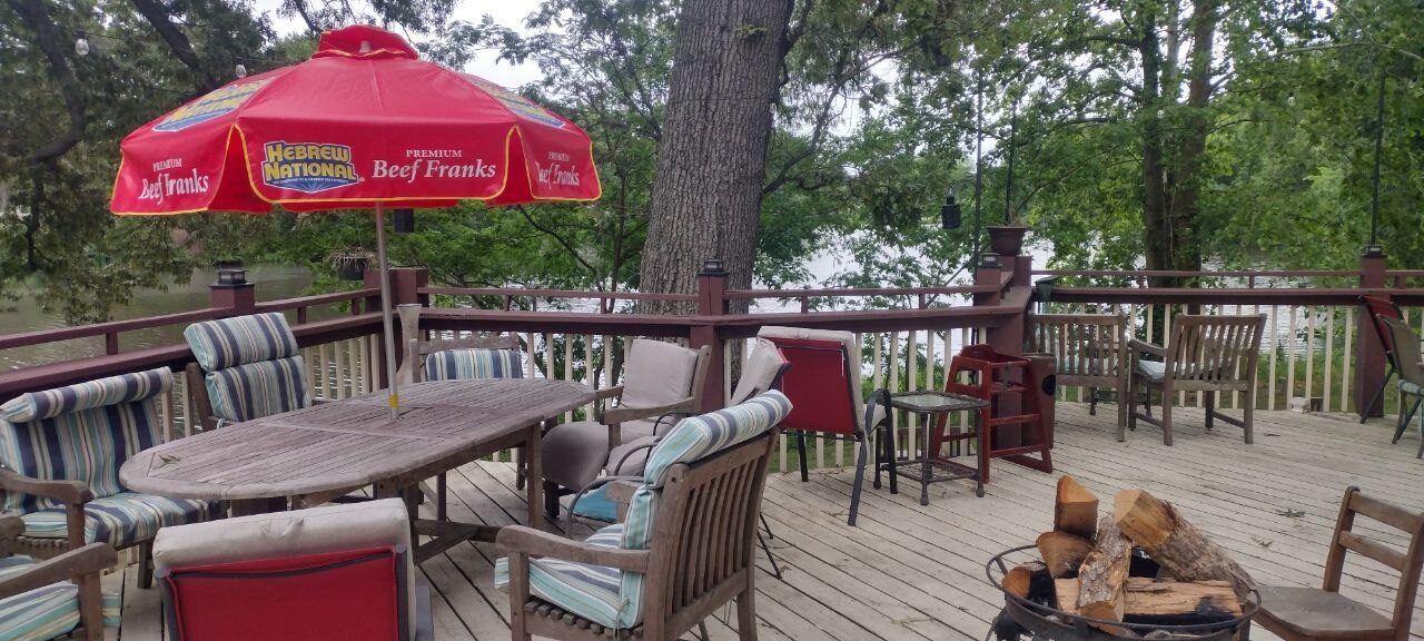 Pemberton Coffeehouse deck overlooking the pond — patio table under a red umbrella, oak trees, and a fire pit at the rail