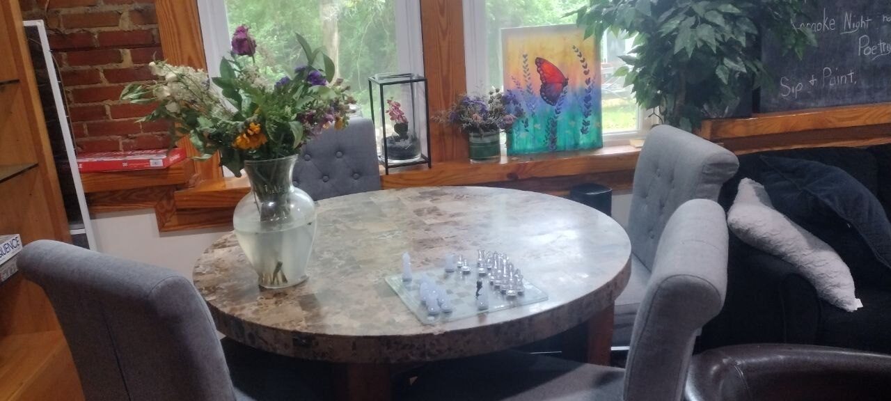 Pemberton Coffeehouse window café seat — marble table with wildflowers and chess set, grey tufted chairs, exposed brick wall