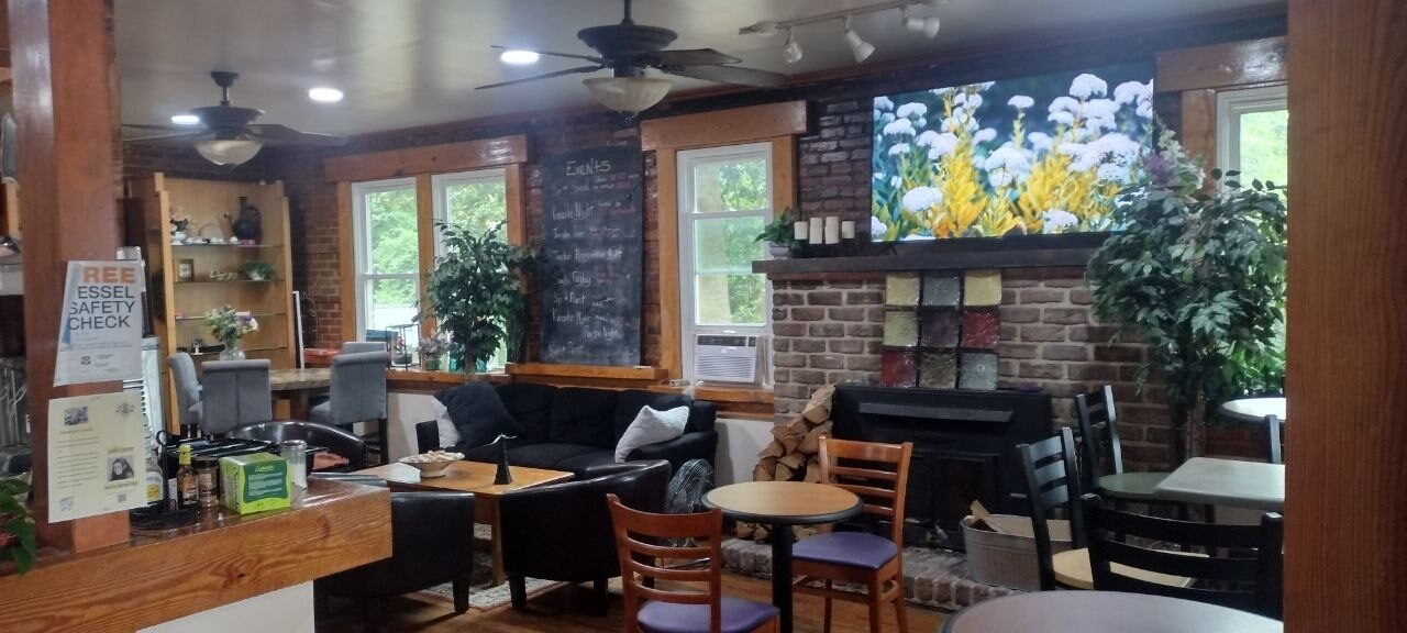 Pemberton Coffeehouse dining room — brick fireplace, wood-burning stove, floral mural over the mantel, events chalkboard on the brick wall