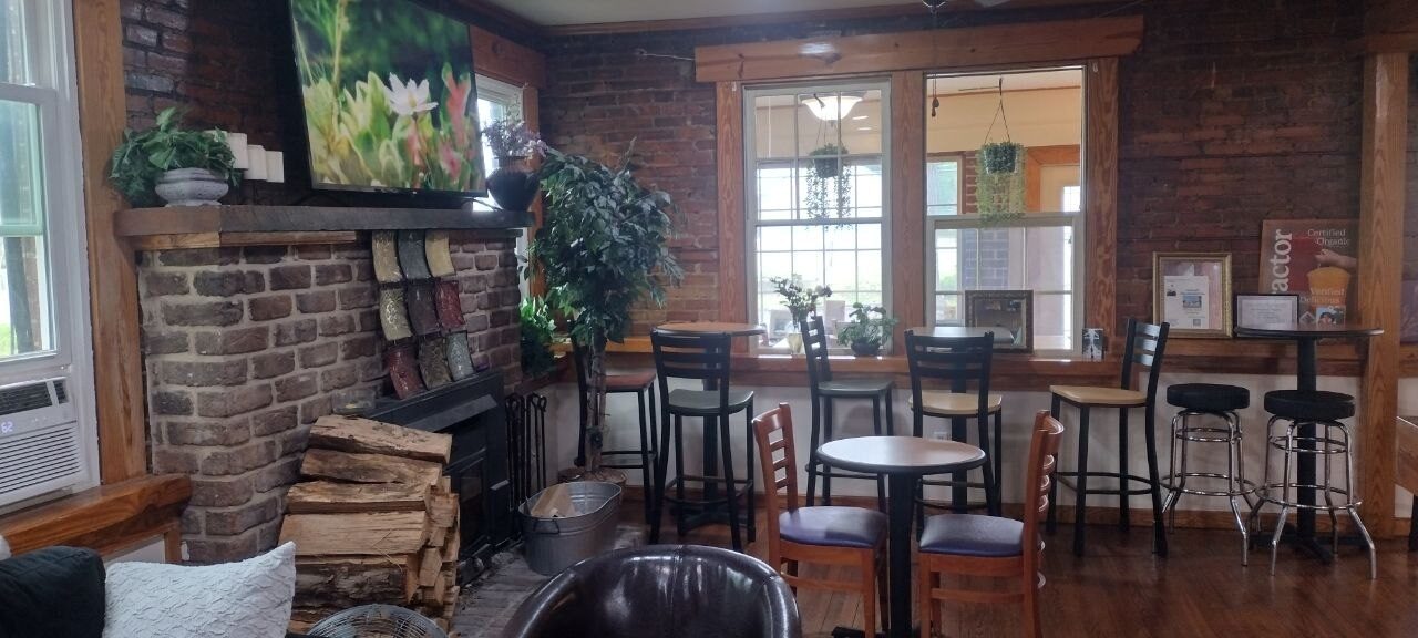 Pemberton Coffeehouse dining room — brick fireplace, bistro tables, mixed wood and metal café chairs