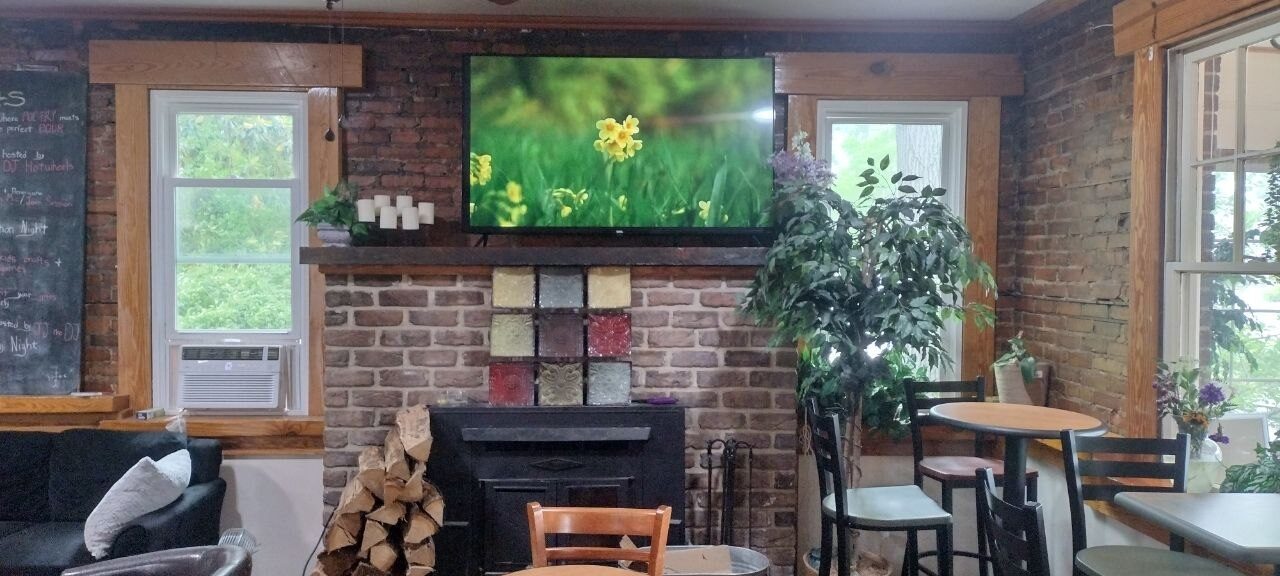 Pemberton Coffeehouse brick fireplace with wood-burning stove, decorative mantel tiles, and a wall-mounted TV