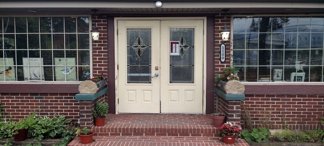 Pemberton Coffeehouse front doors at 1100 Pemberton Drive — leaded-glass white double doors flanked by potted flowers and coach lights
