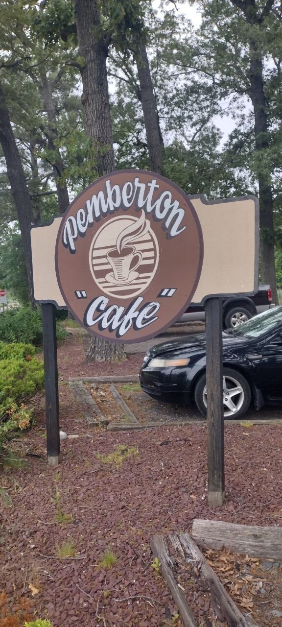 Pemberton Cafe roadside sign — cursive lettering over an illustrated coffee cup on a wood-post sign in a mulch bed